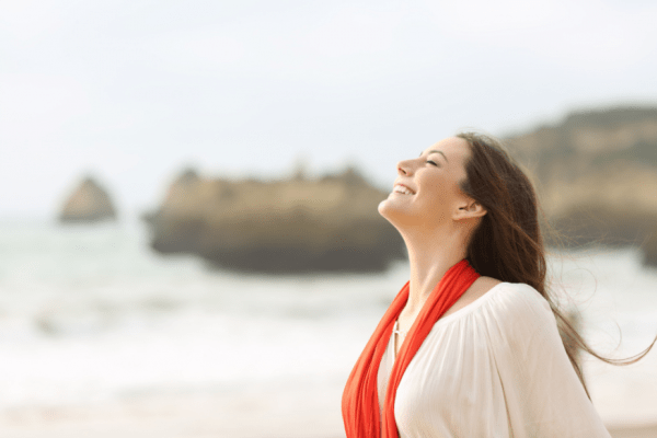 woman smiling, eyes closed, face to the sky, in a beach setting